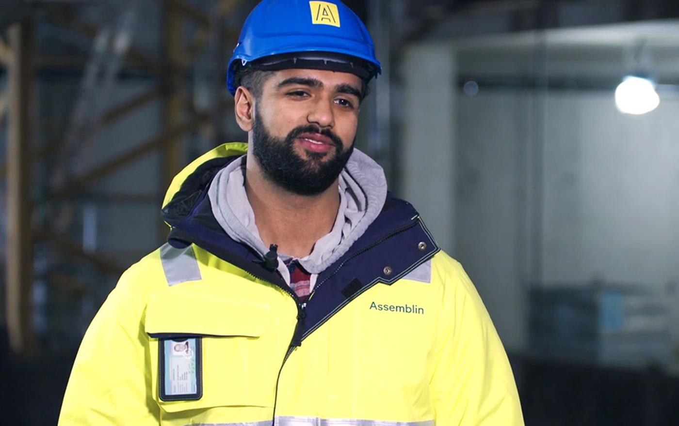 Anställd man med mörka drag, stående i arbetskläder och hjälm