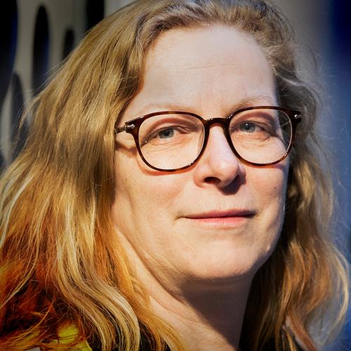 Kvinna med lockigt hår och glasögon tittar mot kameran